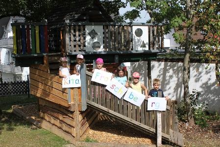 Kinder die auf einem Spielturm stehen und Buchstabenschilder in der Hand halten