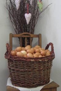 Im Fokus ist ein Flechtkorb mit braunen Eiern, der auf einem Stuhl steht. Im Hintergrund sind dünne Äste mit 3 Herzen als Deko.