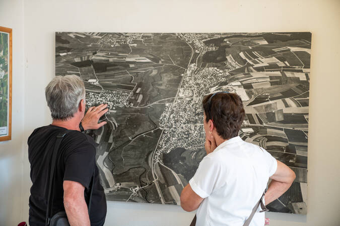 Zwei Personen betrachten aufmerksam eine große, an der Wand hängende schwarz-weiß Karte oder ein Luftbild.