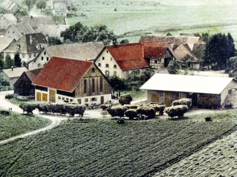 Ein Luftbild von früher auf dem Höfe zu sehen sind und Anhänger voller Heu