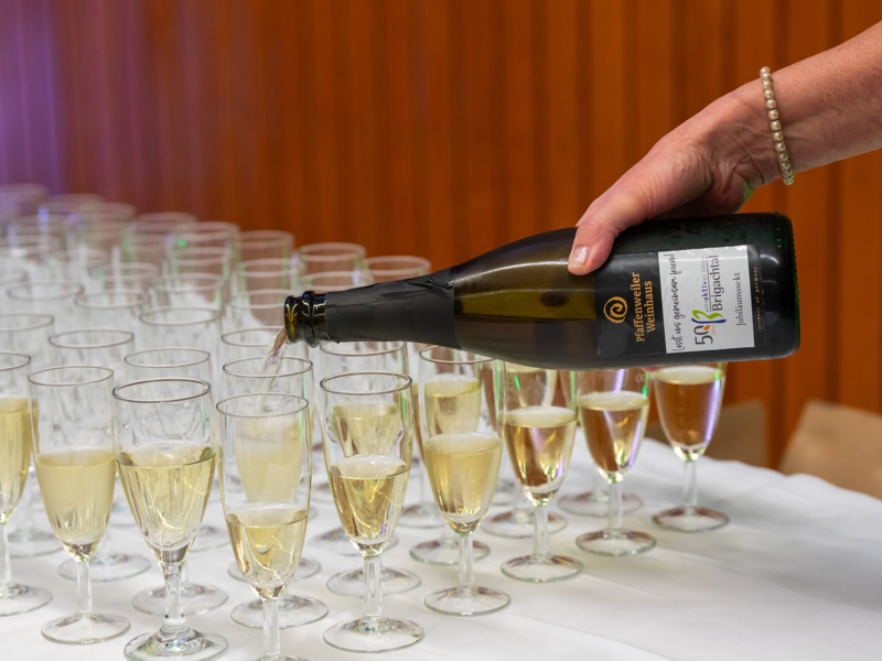 Viele Sektgläser auf einem Tisch und ein Arm der mit einer Sektflasche Sekt in die Gläser eingießt