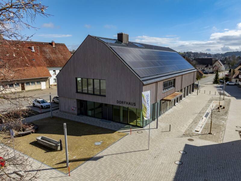 ein Luftbild vom Dorfhaus in Überauchen, der Dorfplatz is zu sehen und der blaue Himmel