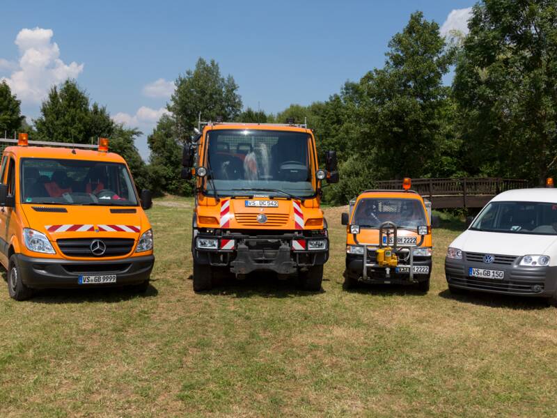 Vier verschiedene Fahrzeuge mit Warnmarkierungen stehen nebeneinander auf einer Wiese bei Tageslicht.