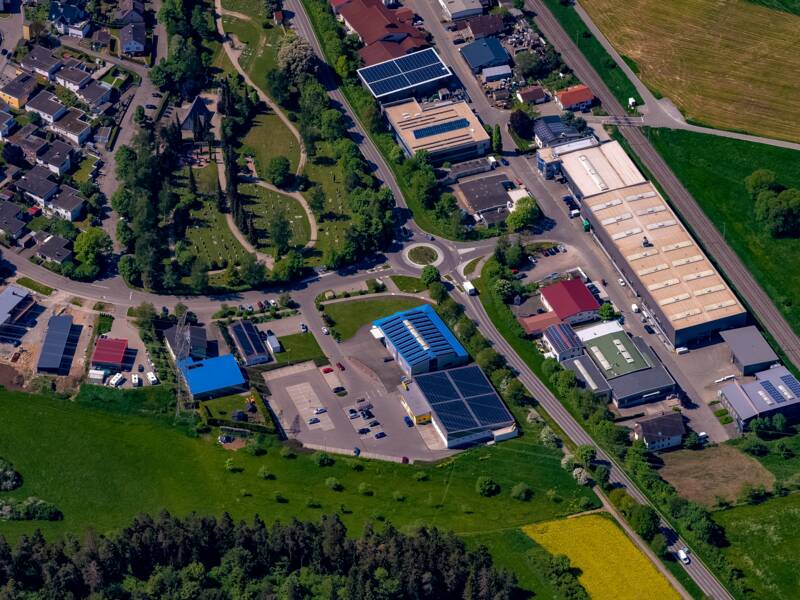 Luftaufnahme einer kleinstädtischen Siedlung mit einer Mischung aus Wohngebäuden, Industrieanlagen und umgebender grüner Landschaft.