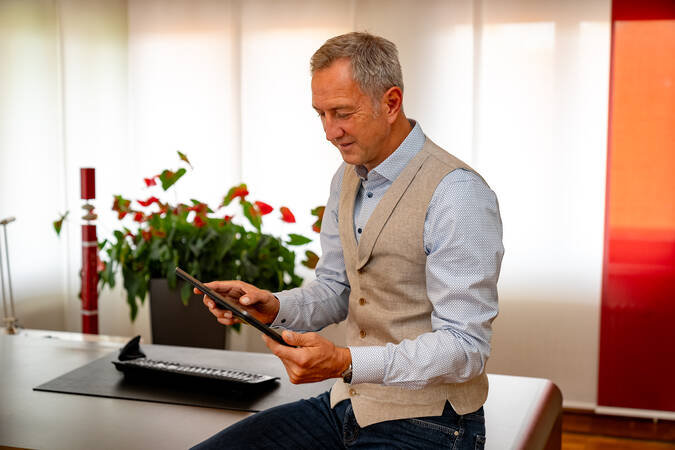 Bürgermeister Michael Schmitt sitzt halb auf seinem Schreibtisch und schaut auf sein Tablet