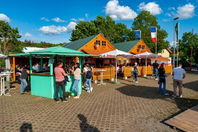 Besuch vom Dorffest stehen vor zwei Holzhütten bei sonnigem Wetter