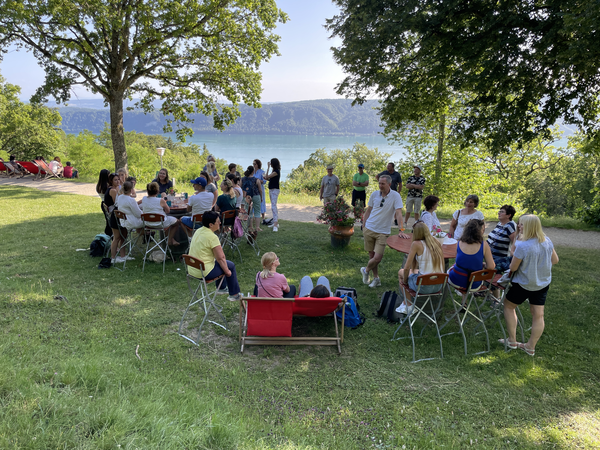 Mitarbeiter sitzen in Gruppen auf einer Wiese mit Stühlen und genießen den Ausblick auf den Bodensee 