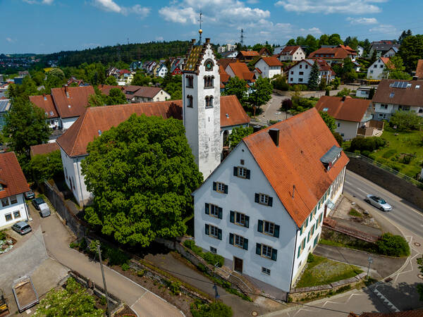 Luftaufnahme der Kirche St. Martin mit einem weißen Fassade und mit rotem Ziegeldach und einem angrenzenden Turm, umgeben von einem Ensemble aus Wohnhäusern und grünen Bäumen.