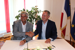 v.l. Bürgermeister Breuille und Bürgermeister Schmitt sitzen am Tisch und reichen sich Hand.