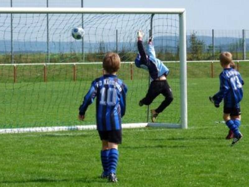 Kinder in blauen Trikots spielen auf einem Rasenplatz Fußball.