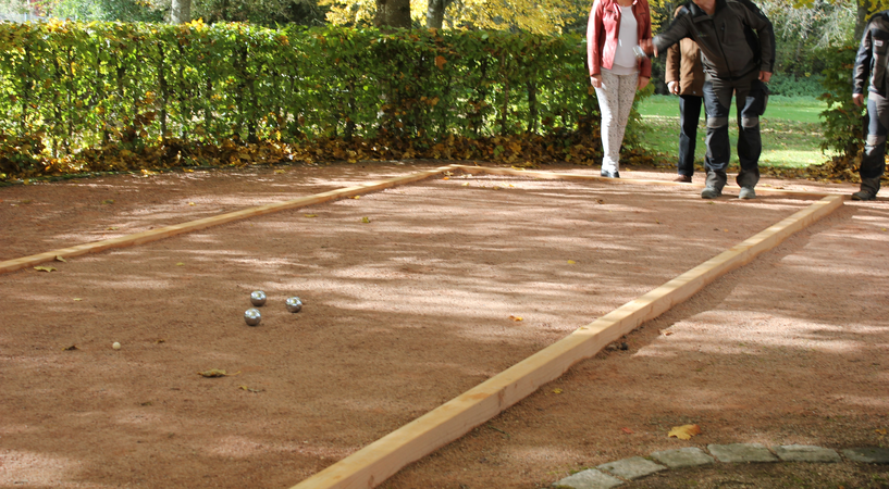 Menschen die Boule-Spielen, drei Kugeln liegen auf dem Feld.