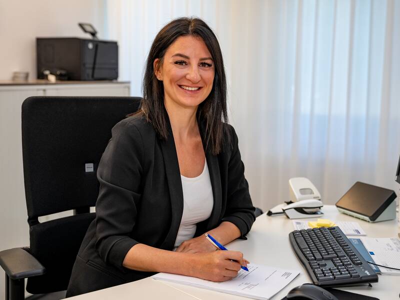 Denise Stöcker sitzt an einem Schreibtisch im Büro und lächelt in die Kamera