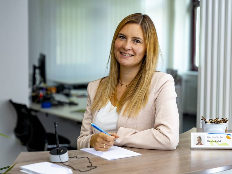 Sandra Zipfel steht in einem Büro und lächelt in die Kamera