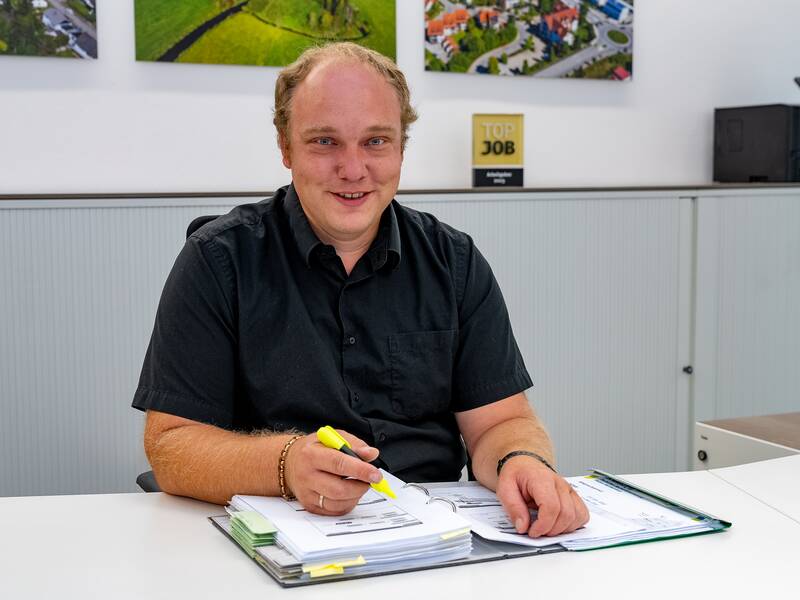 Eric Elsäßer sitzt am Schreibtisch und lächelt in die Kamera