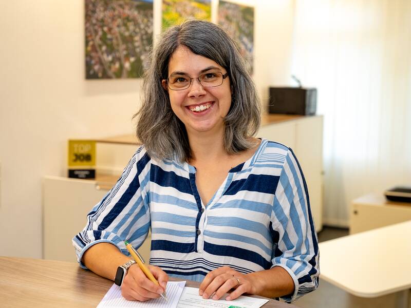 Tanja Schlenker steht im Büro an einer Theke und lächelt in die Kamera