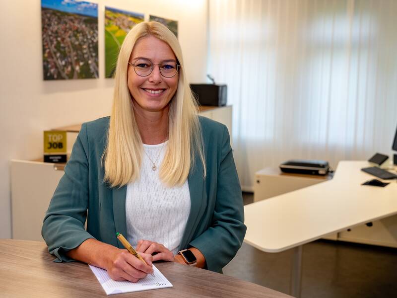 Katja Seng steht im Büro an einer Theke und lächelt in die Kamera