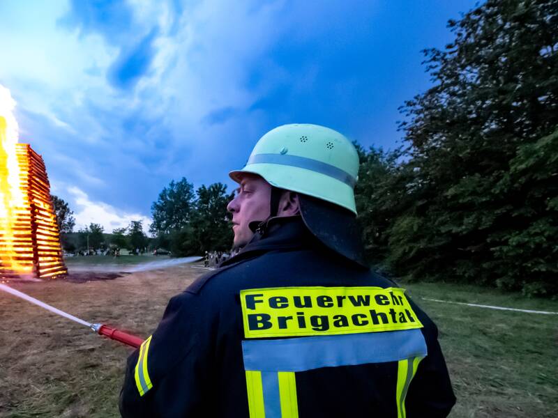 Ein Feuerwehrmann löscht ein großes Feuer auf einem Feld bei Dämmerung.