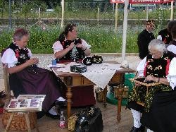 drei Frauen in Trachtenkleidung sitzen zusammen an einem Tisch und sticken.